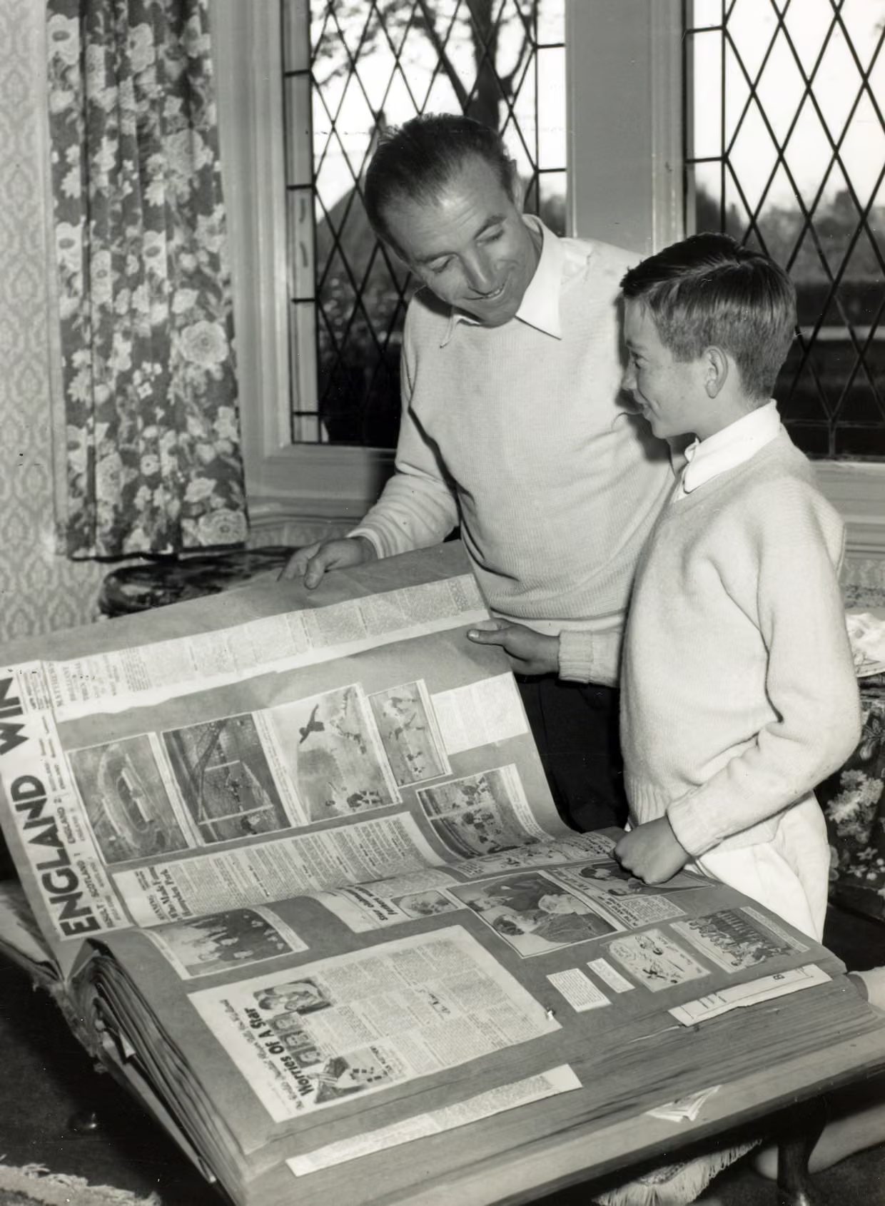Footballer Stanley Matthews and his son smile looking at his football scrapbook